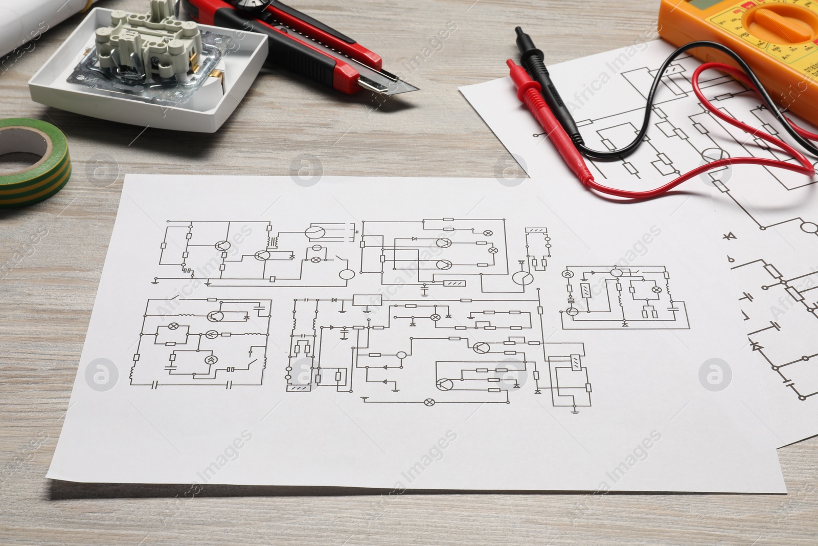 Photo of Wiring diagrams and digital multimeter on white wooden table, closeup
