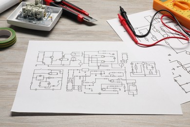 Wiring diagrams and digital multimeter on white wooden table, closeup