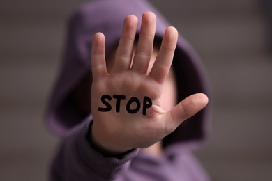 Image of No child abuse. Boy showing hand with written Stop on palm, selective focus
