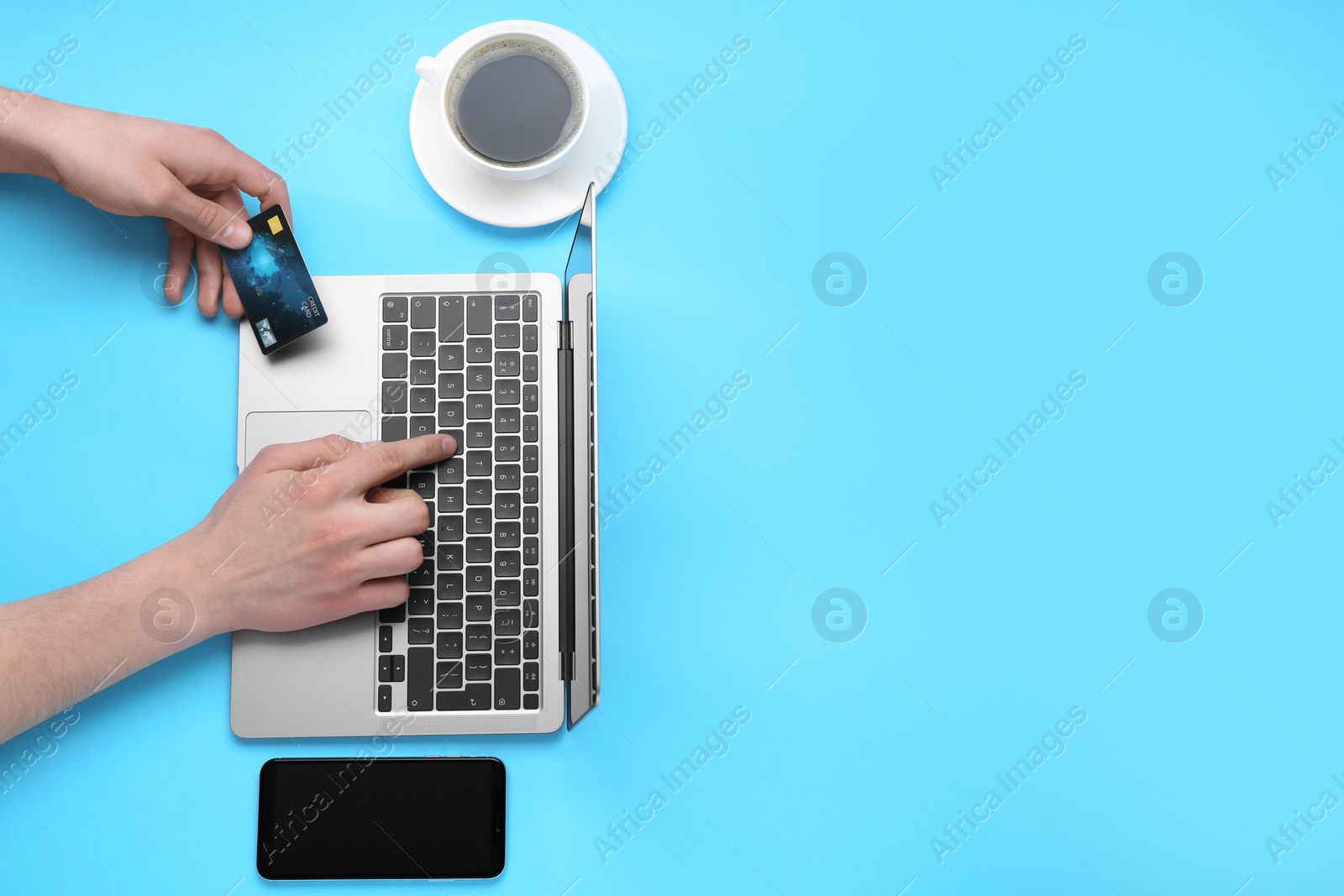 Photo of Online payment. Man with laptop, credit card, smartphone and coffee on light blue background, top view. Space for text