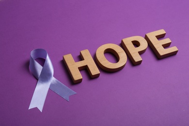 Purple awareness ribbon and word HOPE made of wooden letters on color background