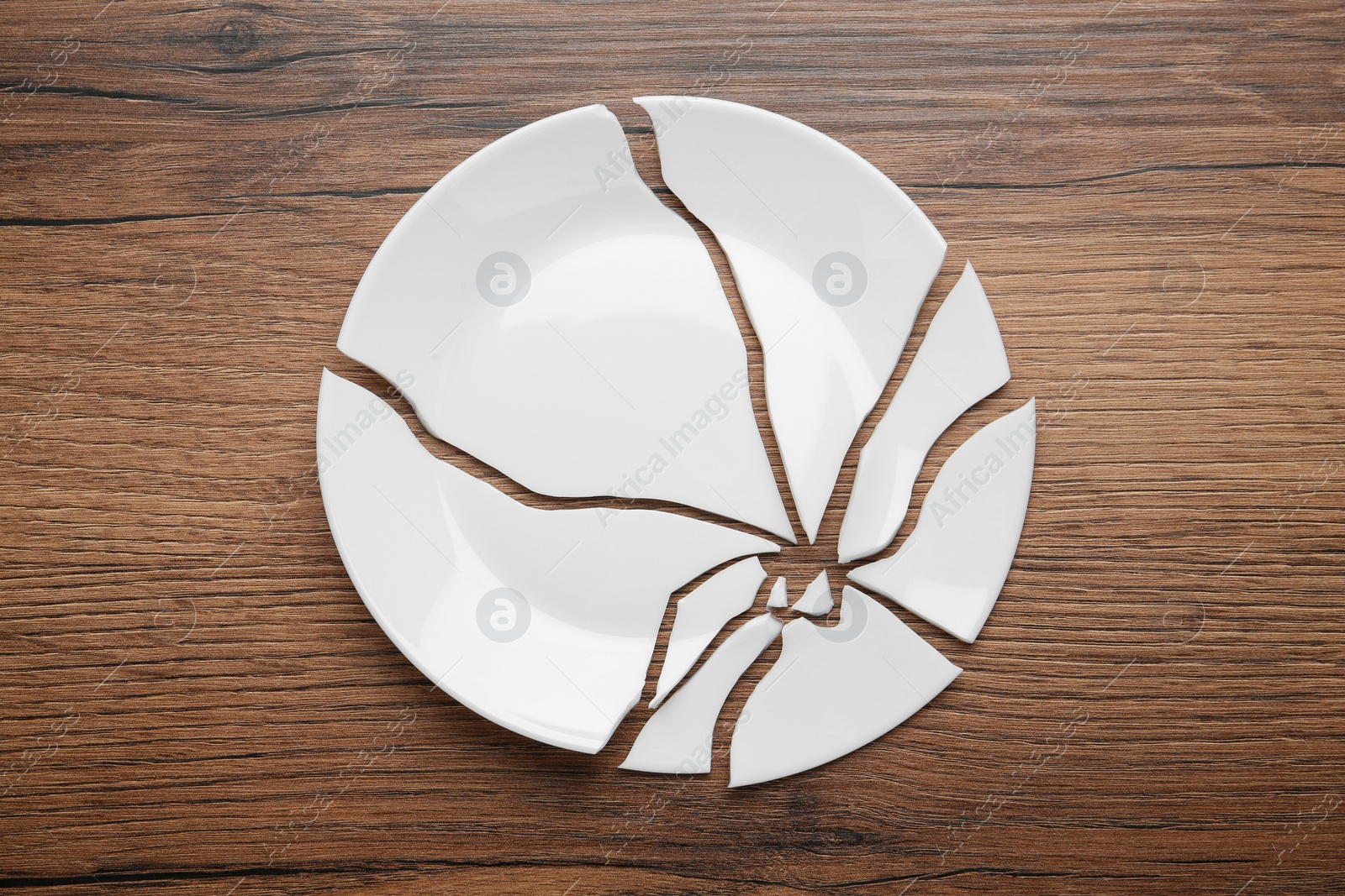 Photo of Pieces of broken ceramic plate on wooden table, flat lay