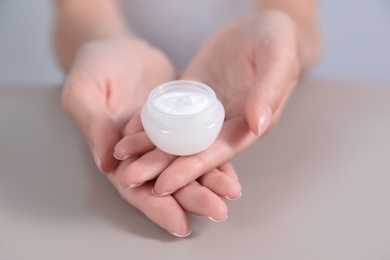 Photo of Young woman holding jar of cream at table, closeup