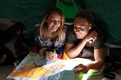 Photo of Young couple in sleeping bags with map and flashlight inside of tent