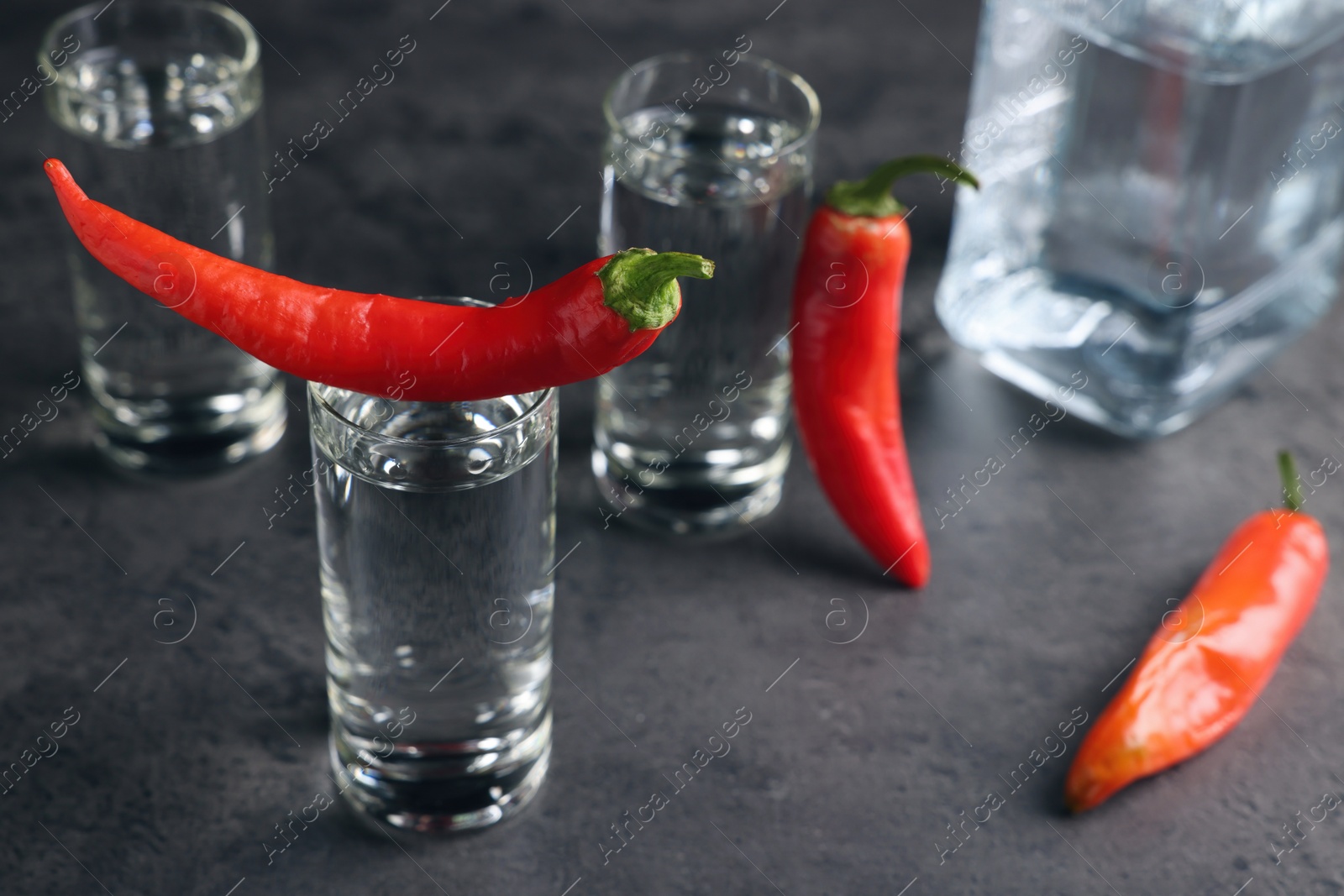 Photo of Red hot chili peppers and vodka on grey table