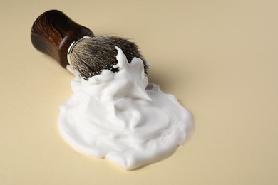 Photo of Brush with shaving foam on beige background, closeup