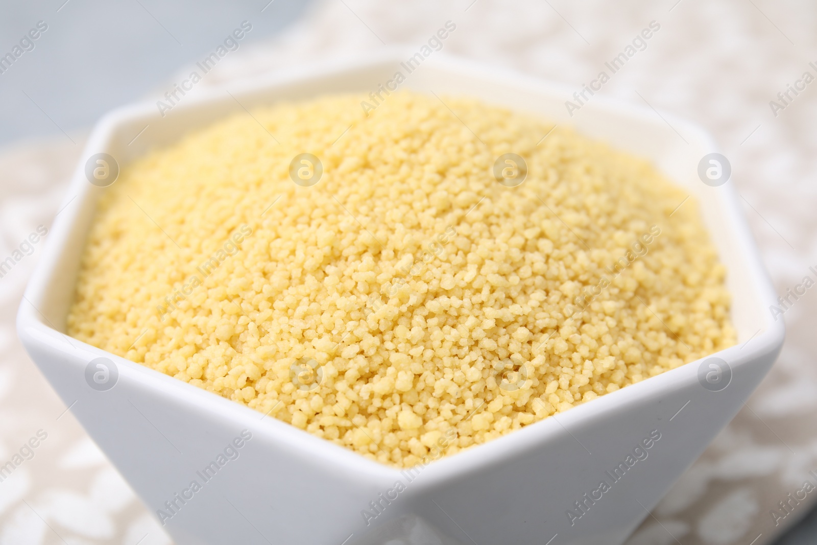 Photo of Raw couscous in bowl on table, closeup