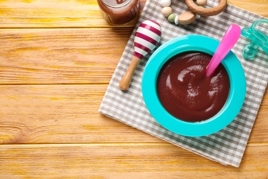 Photo of Flat lay composition with bowl of healthy baby food on wooden table. Space for text