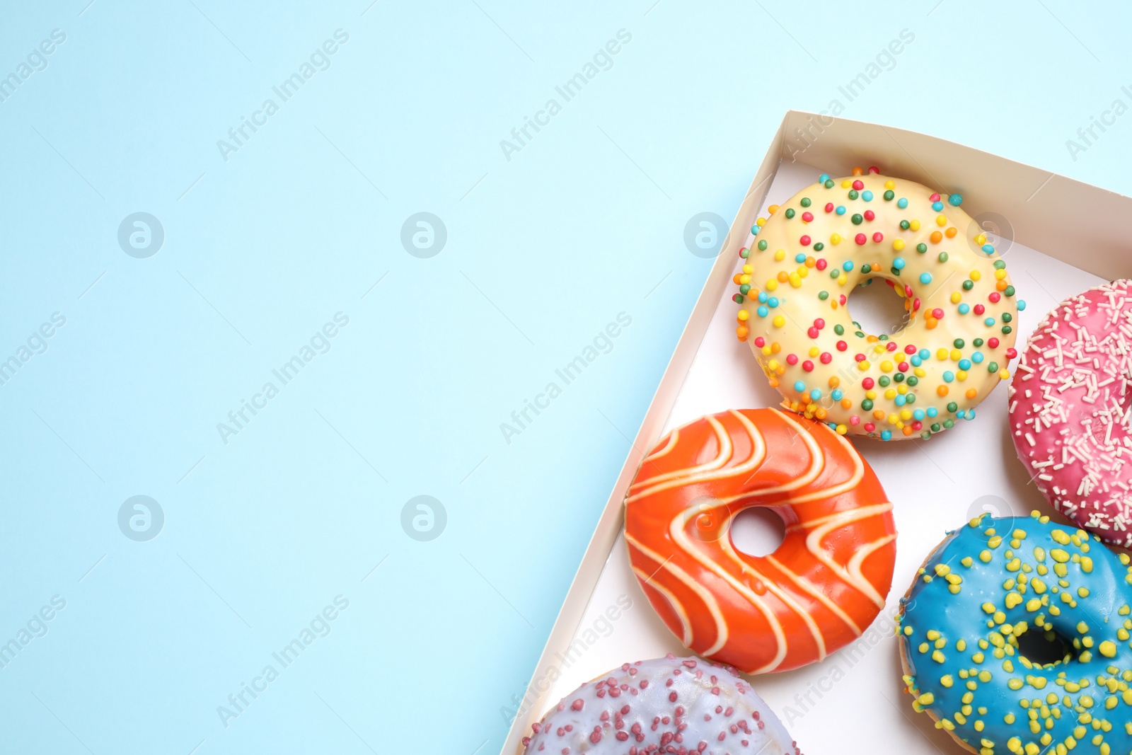 Photo of Delicious glazed donuts on light blue background, top view. Space for text