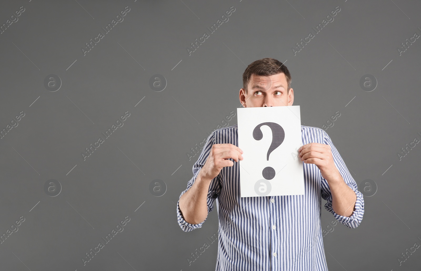 Photo of Emotional man holding paper with question mark on grey background, space for text