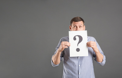 Photo of Emotional man holding paper with question mark on grey background, space for text