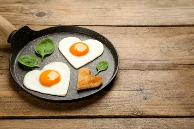 Heart shaped fried eggs with toast in frying pan on wooden table, space for text
