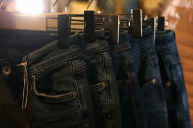 Photo of Modern jeans hanging on clothing rack in shop, closeup
