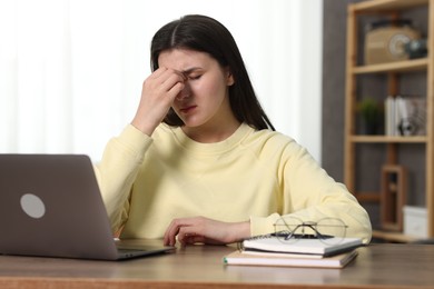 Overwhelmed woman sitting with laptop at table indoors