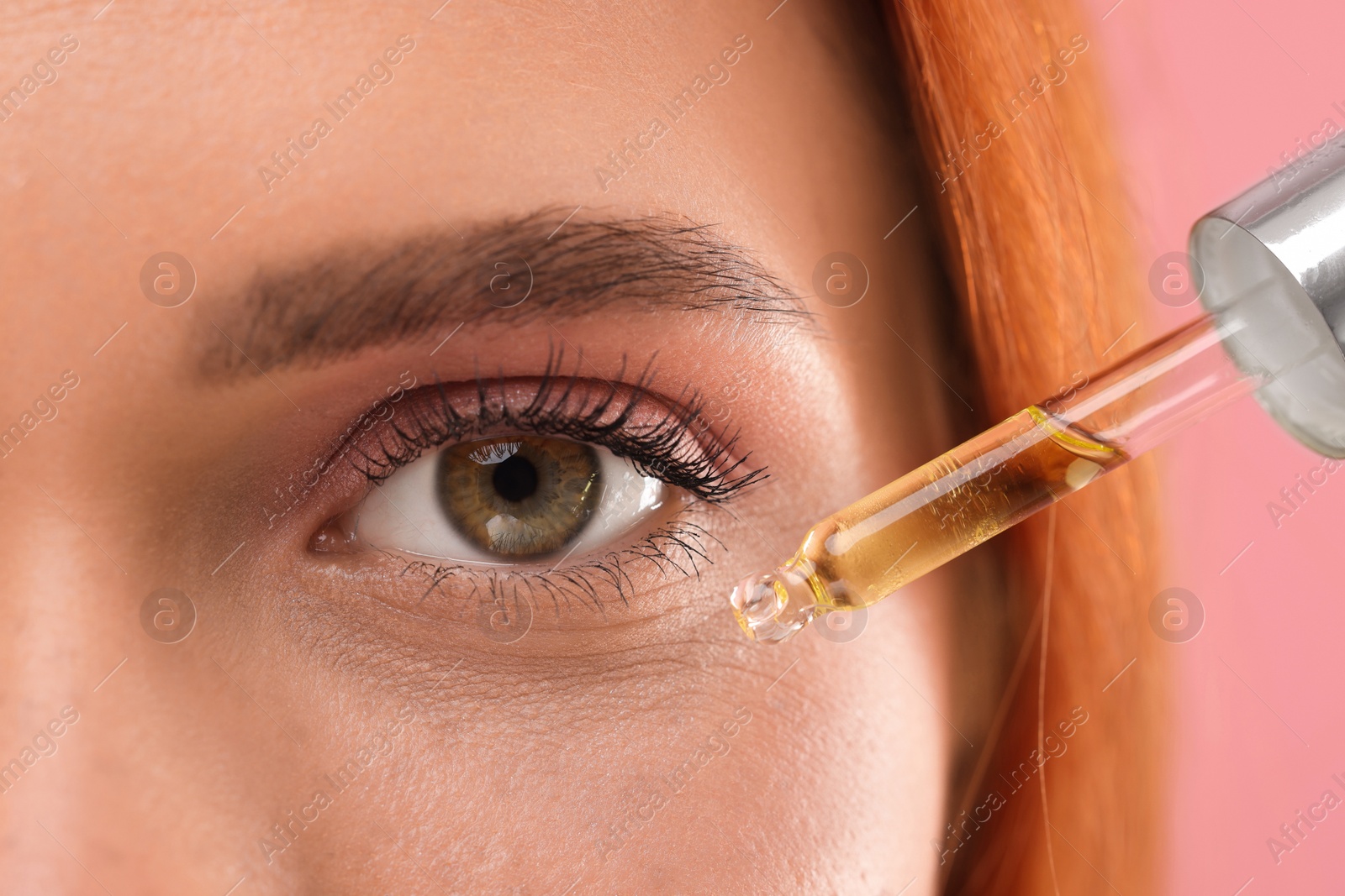 Photo of Beautiful young woman applying cosmetic serum onto her face on pink background, closeup