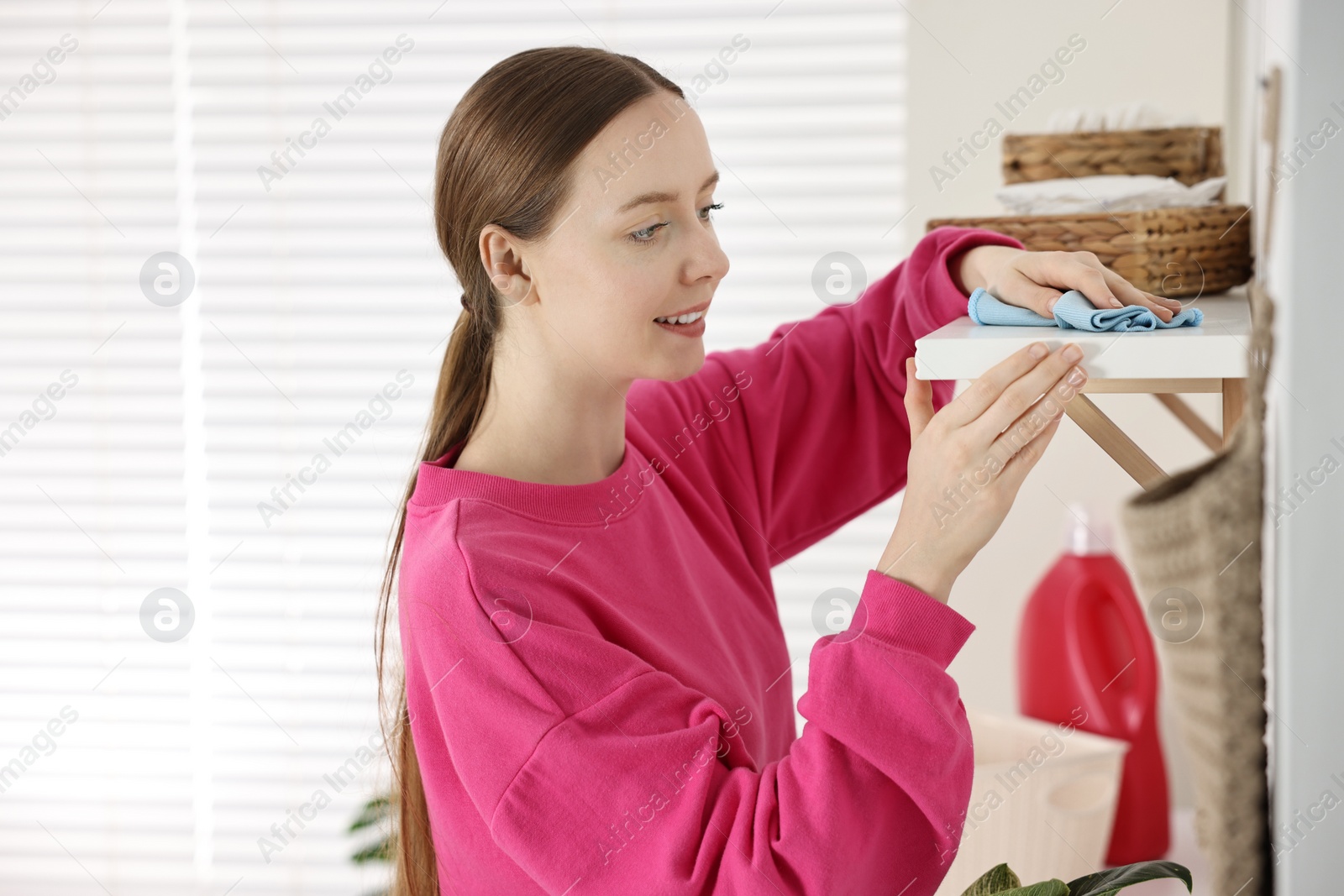 Photo of Woman cleaning shelf with rag at home, space for text