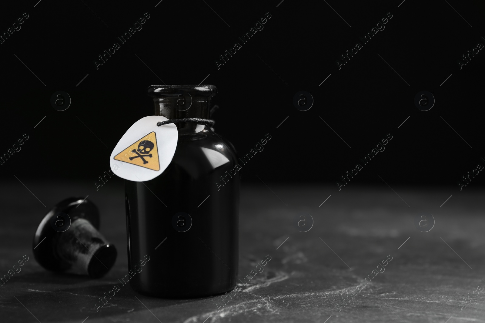 Photo of Open glass bottle of poison with warning sign on black table. Space for text