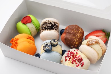 Photo of Cardboard box with delicious sweet macarons on white table, closeup