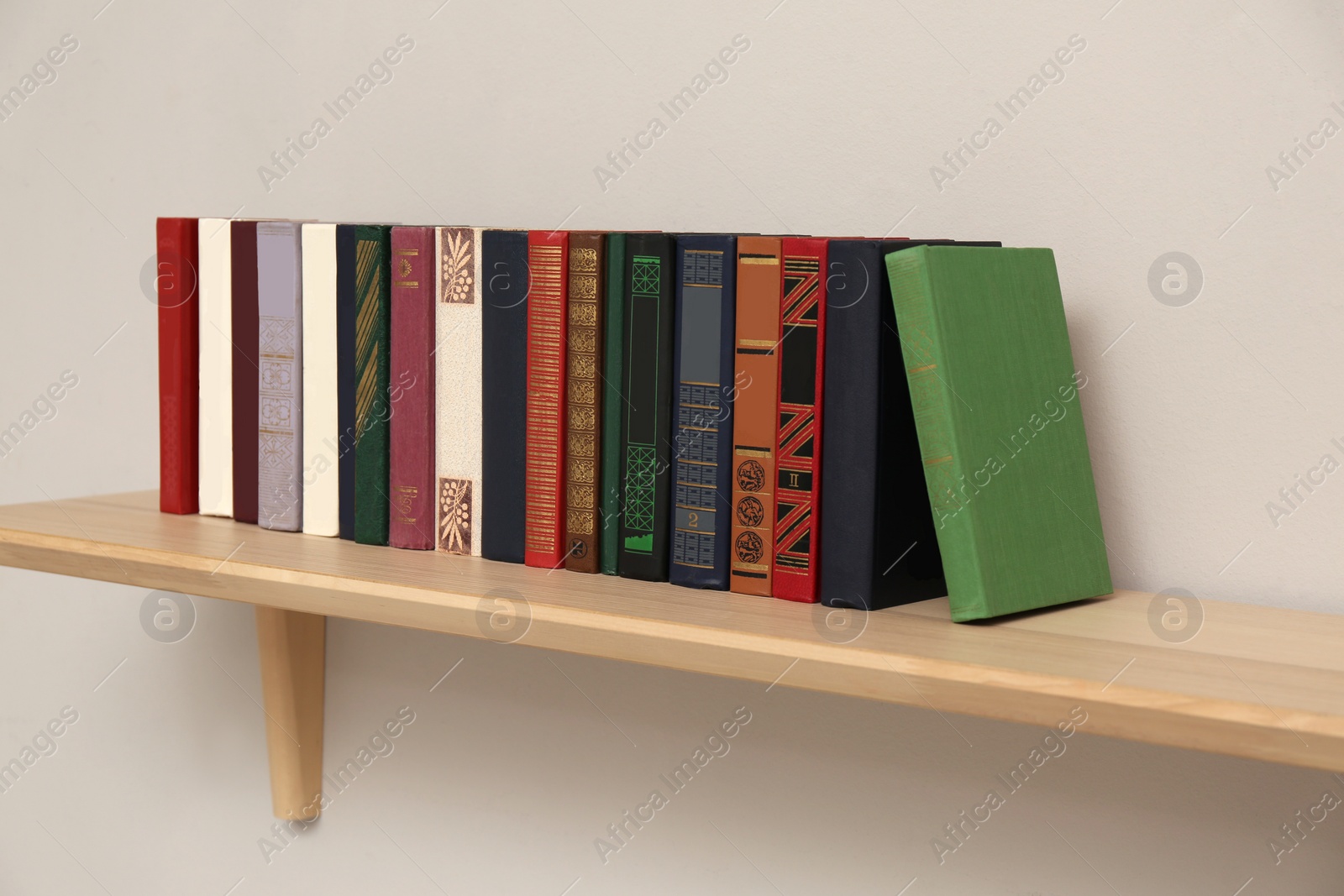 Photo of Wooden shelf with different books on light wall