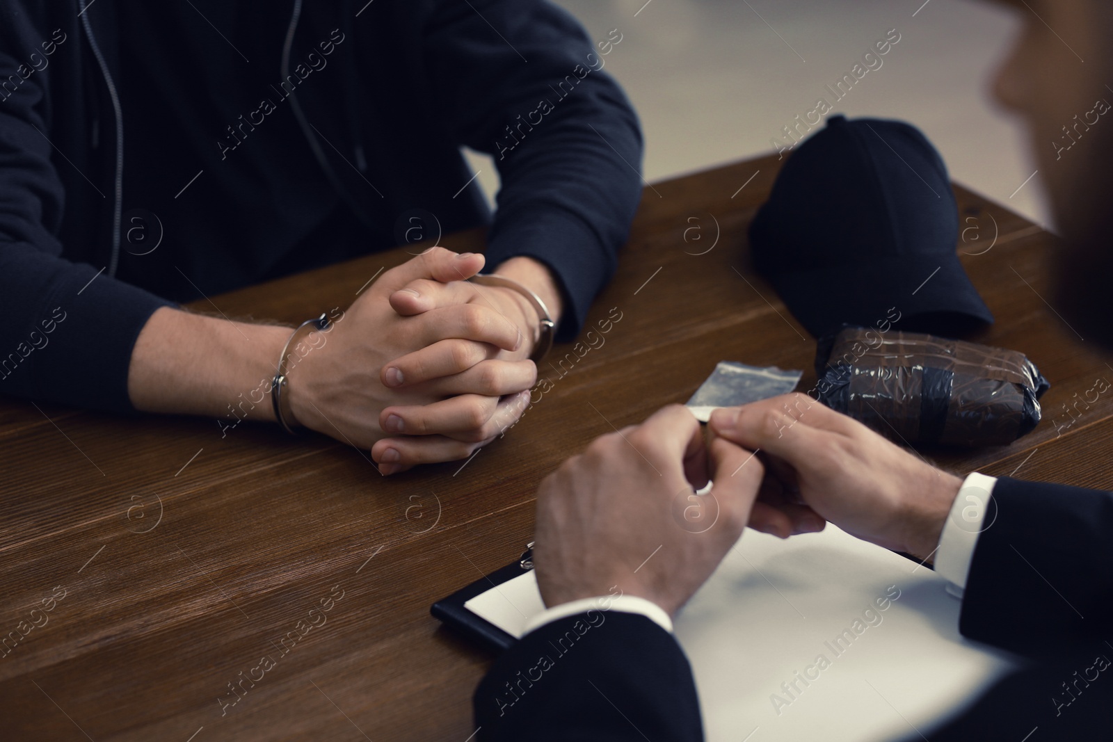 Photo of Police officer interrogating criminal in handcuffs at desk indoors