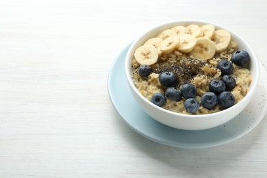 Tasty oatmeal with banana, blueberries and chia seeds served in bowl on white wooden table, space for text