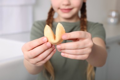 Girl holding tasty fortune cookie with prediction indoors, closeup