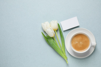 White tulips, coffee and blank card on light blue background, flat lay with space for text. Good morning