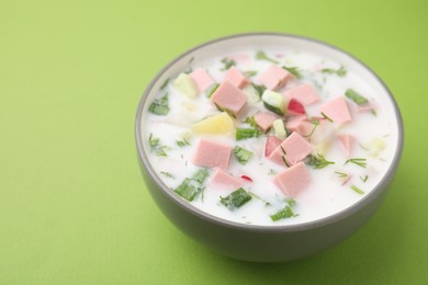 Delicious cold summer soup (okroshka) with boiled sausage in bowl on green table. Space for text