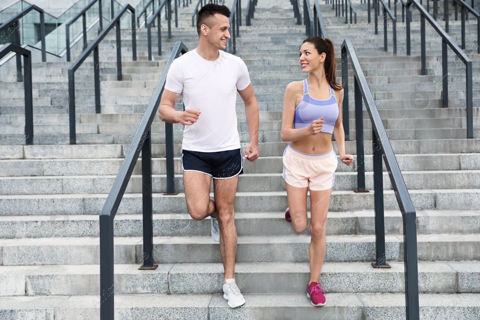 Photo of Man and woman in fitness clothes running downstairs outdoors