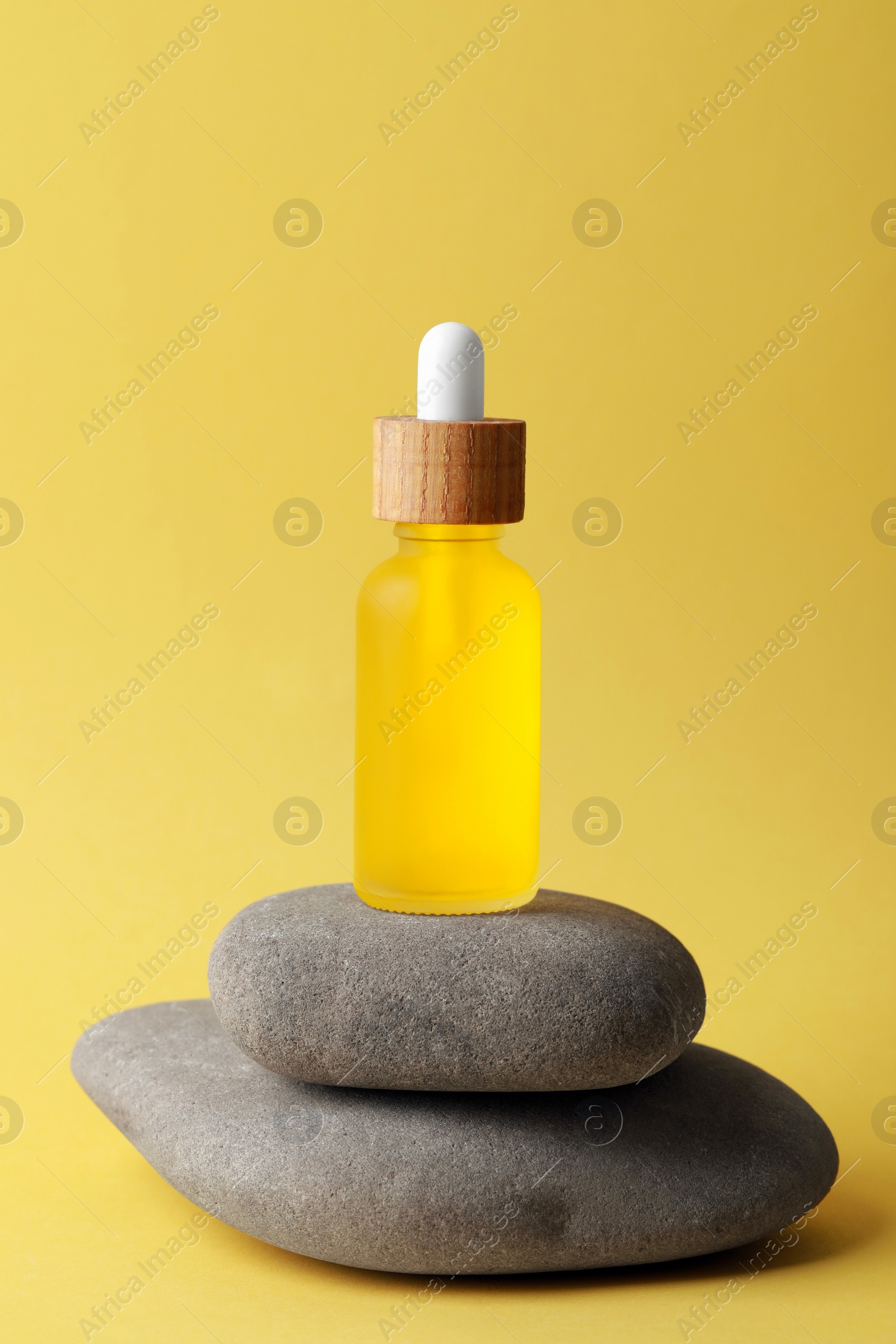 Photo of Bottle of face serum and spa stones on yellow background