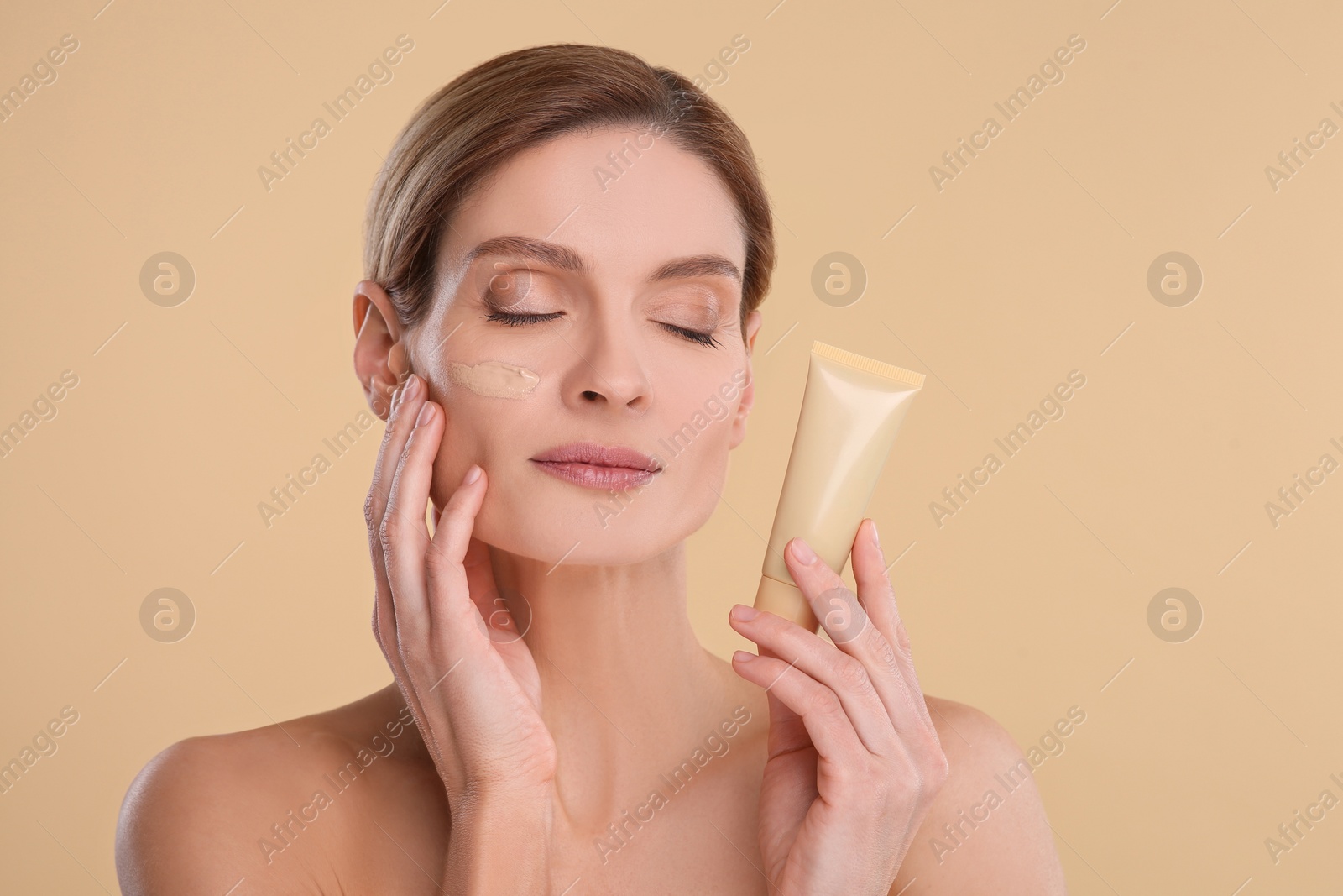 Photo of Woman holding tube of foundation on beige background