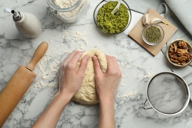 Photo of Woman kneading dough at white marble table, top view. Making delicious pesto bread