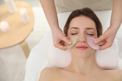 Young woman receiving facial massage with gua sha tools in beauty salon