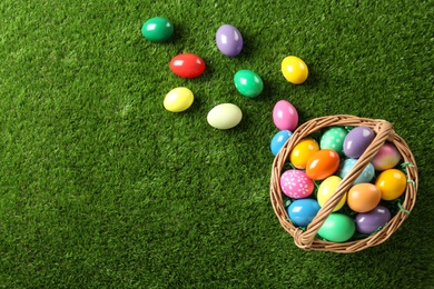 Photo of Wicker basket with Easter eggs on green grass, flat lay. Space for text