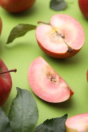 Photo of Tasty apples with red pulp and leaves on light green background, closeup