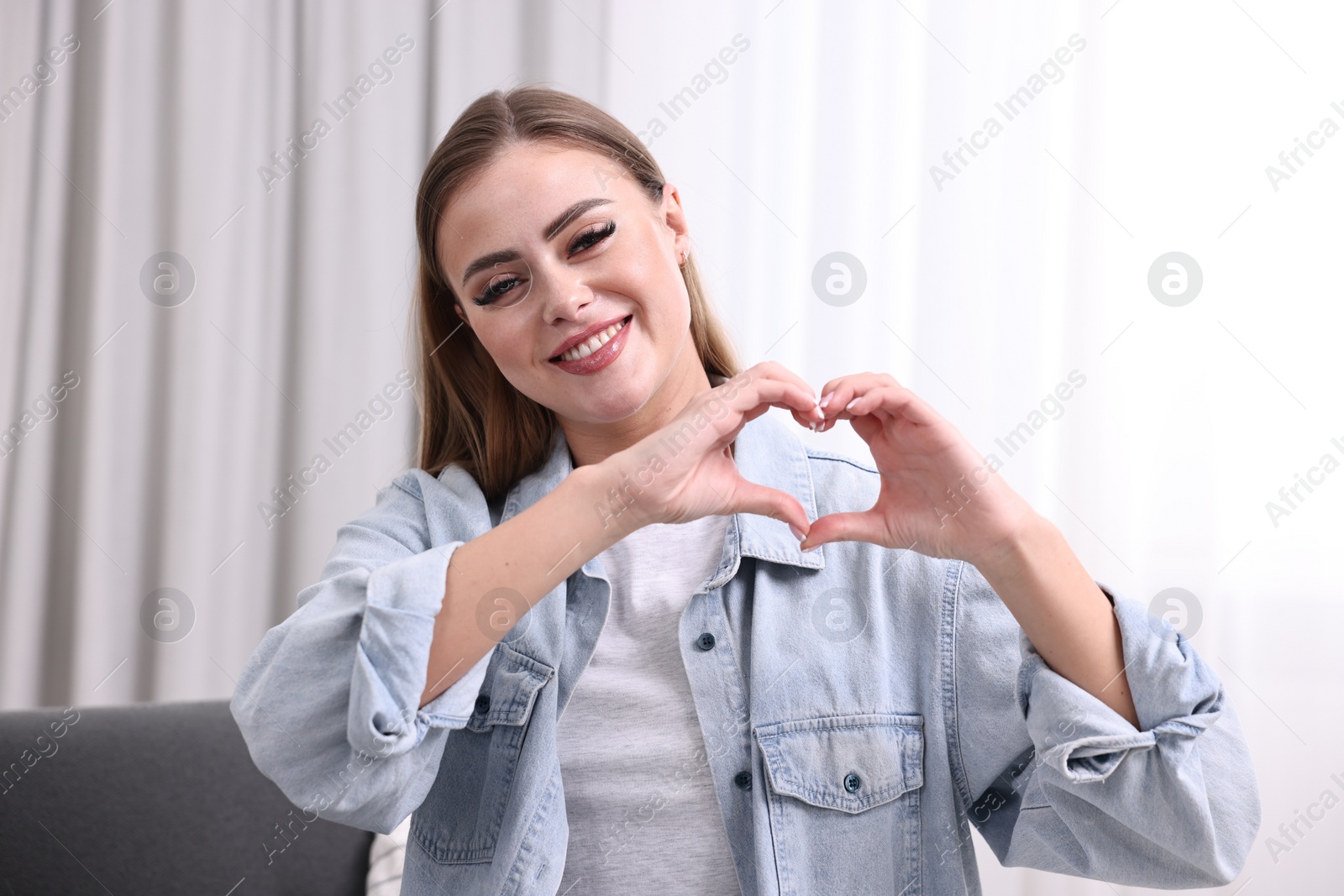 Photo of Happy woman showing heart gesture with hands indoors