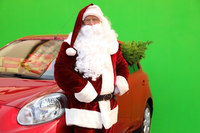 Photo of Authentic Santa Claus near car with fir tree and presents against green background