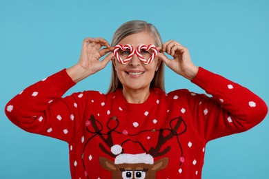 Senior woman in Christmas sweater and funny glasses on light blue background