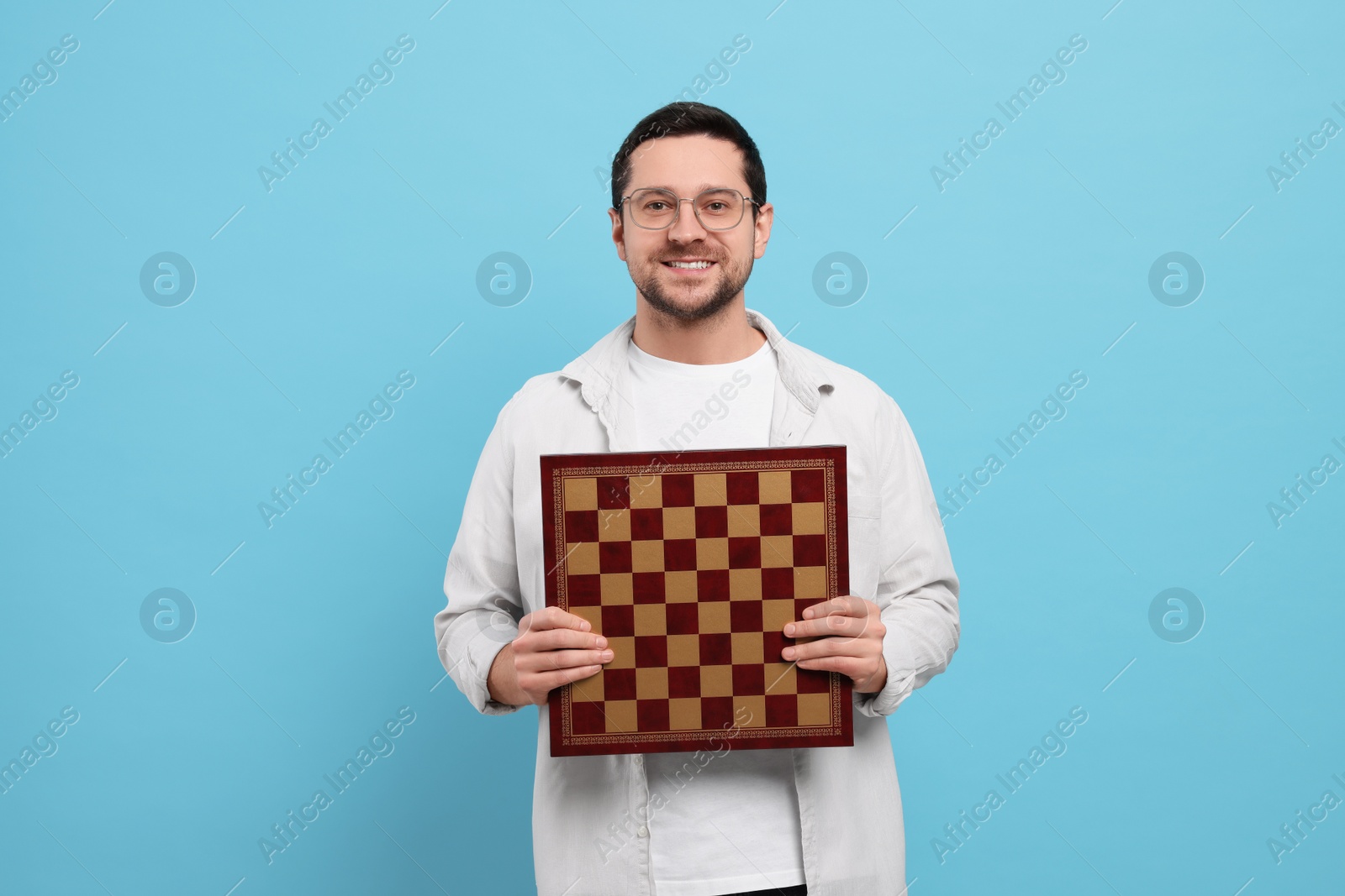 Photo of Handsome man holding chessboard on light blue background