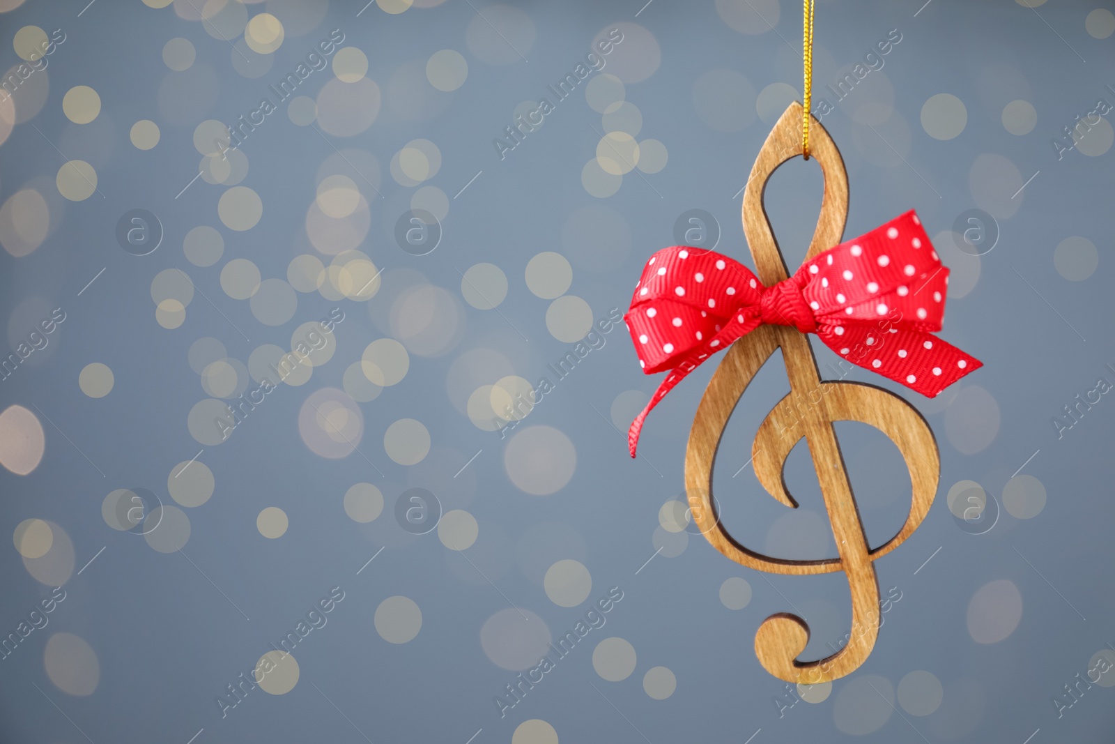 Photo of Wooden music note with red bow hanging on light blue background with Christmas lights. Space for text