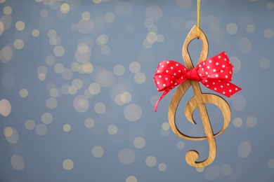 Photo of Wooden music note with red bow hanging on light blue background with Christmas lights. Space for text