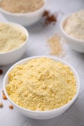 Bowls with different types of flour on tiled table, closeup