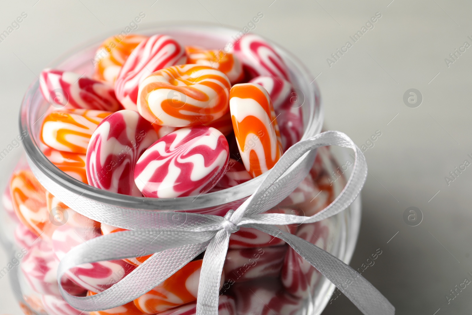 Photo of Sweet candies in glass jar on light grey table, closeup