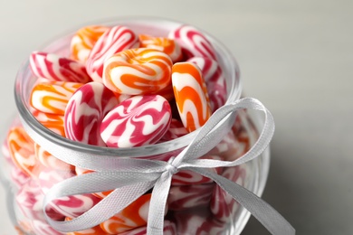 Sweet candies in glass jar on light grey table, closeup