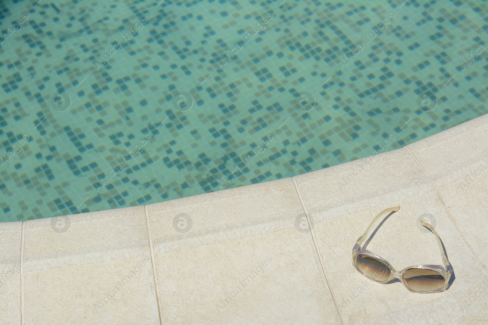 Photo of Stylish sunglasses near outdoor swimming pool on sunny day, space for text. Beach accessory