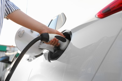 Photo of Woman inserting plug into electric car socket at charging station, low angle view