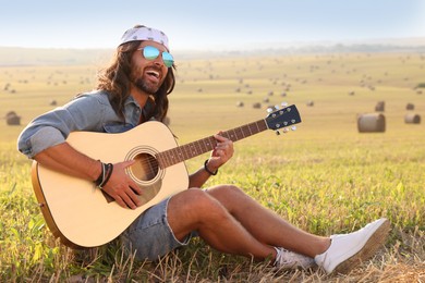 Photo of Handsome happy hippie man playing guitar in field