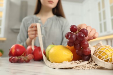 Photo of Woman taking grapes out from string bag at light marble table, closeup