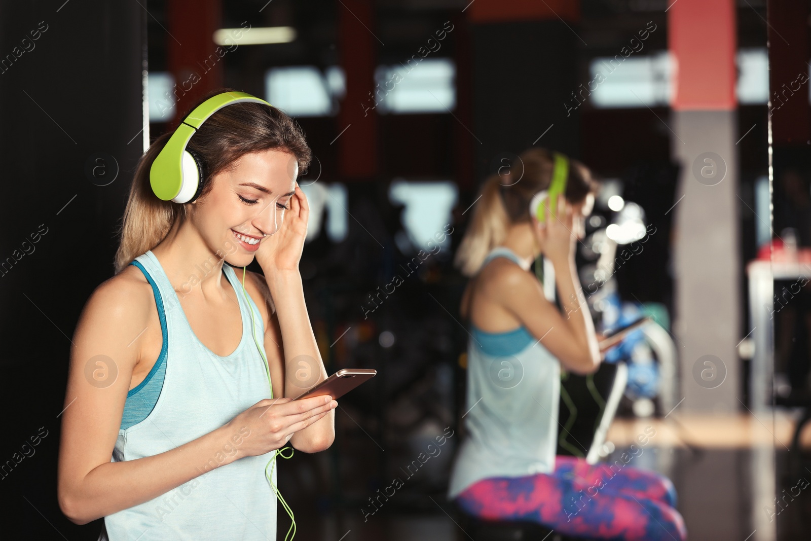 Photo of Young woman with headphones listening to music on mobile device at gym