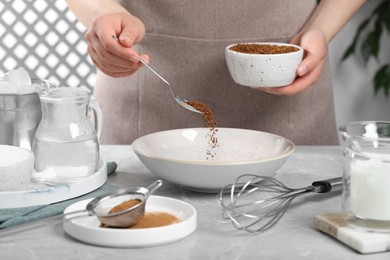 Photo of Making dalgona coffee. Woman pouring instant granules into bowl at light gray table, closeup